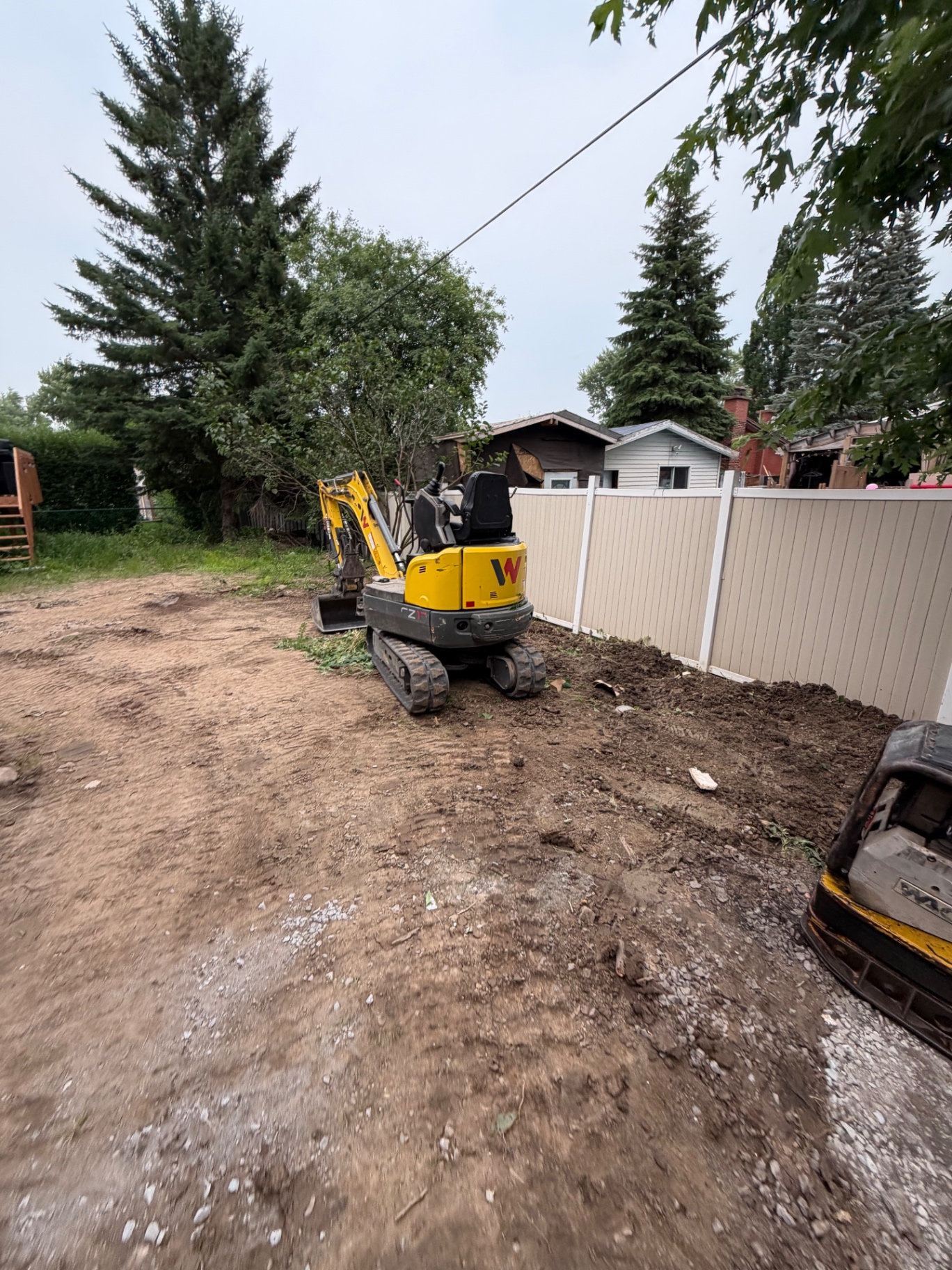 Mini-excavatrice sur un chantier résidentiel, terrain excavé et nivelé le long d'une clôture